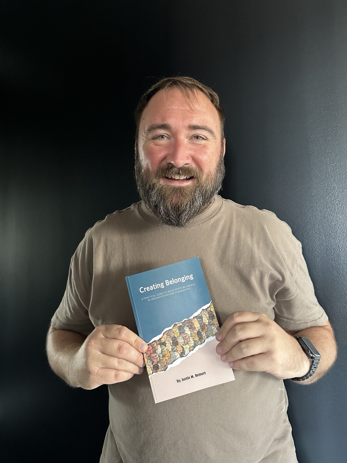 Justin Reinert holding his book Creating Belonging